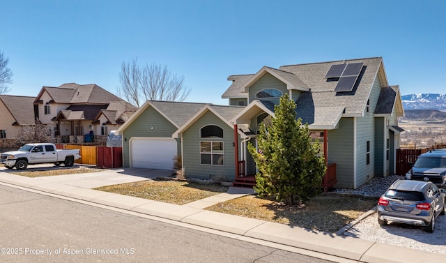 view of front of property featuring roof mounted solar panels, fence, roof with shingles, concrete driveway, and an attached garage