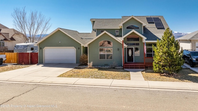 traditional home featuring fence, roof with shingles, solar panels, concrete driveway, and a garage