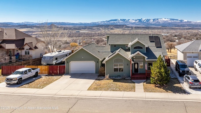 traditional-style home with fence, concrete driveway, a garage, a mountain view, and roof mounted solar panels