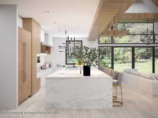 interior space featuring white cabinets, light stone countertops, light hardwood / wood-style flooring, and an island with sink