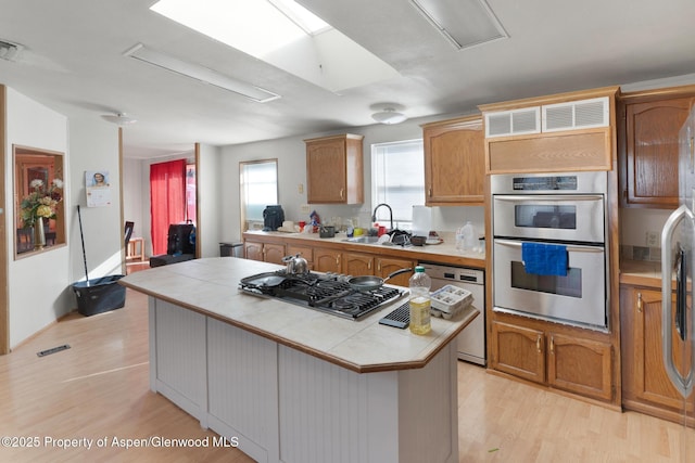 kitchen featuring sink, light hardwood / wood-style flooring, stainless steel appliances, a center island, and tile counters