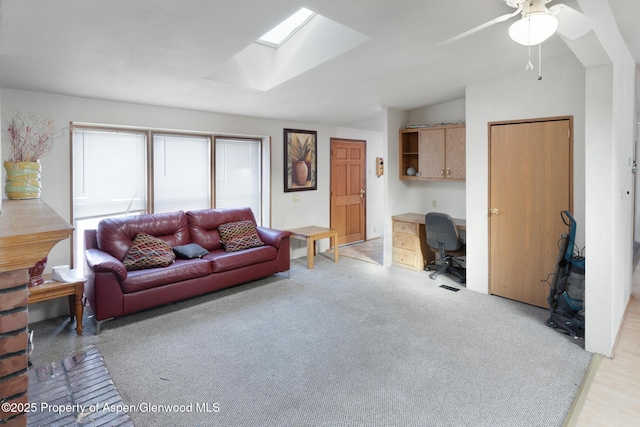 living room with lofted ceiling with skylight, light colored carpet, and ceiling fan