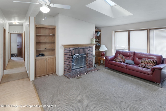 living room featuring a brick fireplace, vaulted ceiling with skylight, and ceiling fan