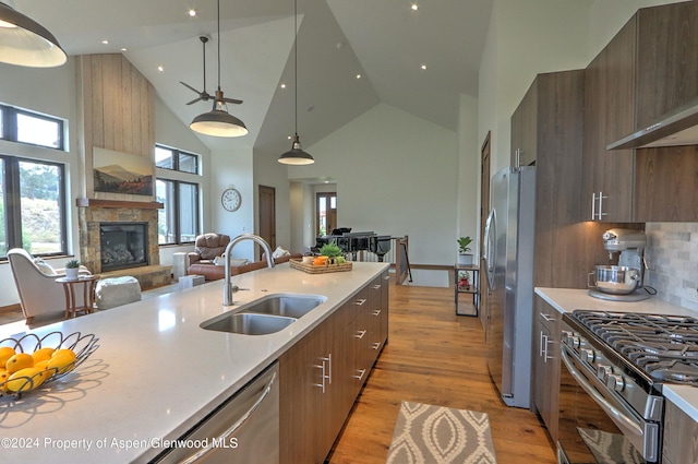 kitchen with sink, a stone fireplace, high vaulted ceiling, pendant lighting, and appliances with stainless steel finishes