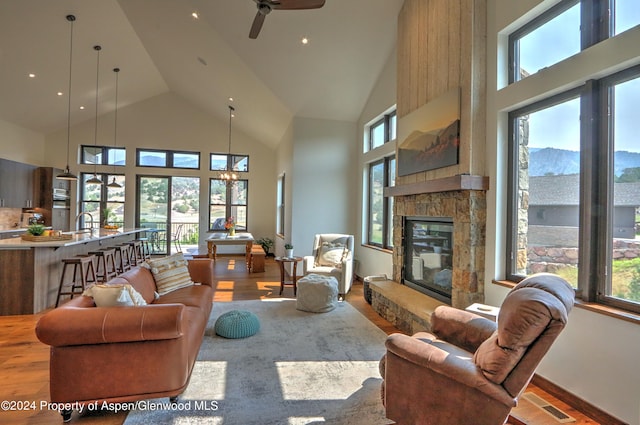 living room featuring a fireplace, a towering ceiling, wood-type flooring, and ceiling fan with notable chandelier