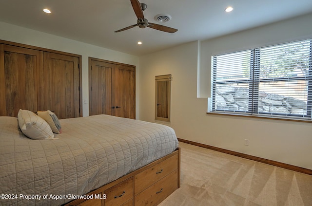 bedroom featuring ceiling fan, light colored carpet, and two closets