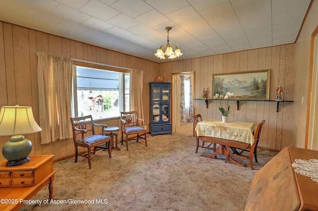 dining room featuring carpet, wooden walls, and a notable chandelier