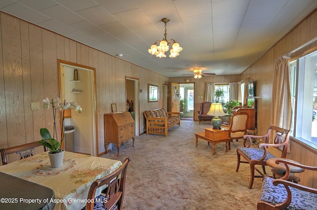 carpeted living area featuring a healthy amount of sunlight, wood walls, and ceiling fan with notable chandelier