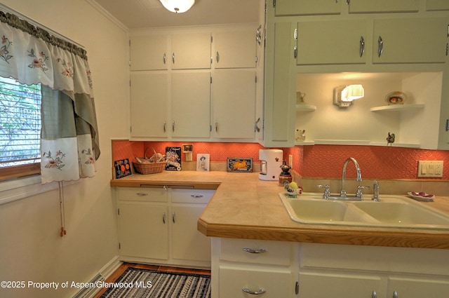 kitchen with a sink, open shelves, white cabinetry, backsplash, and light countertops