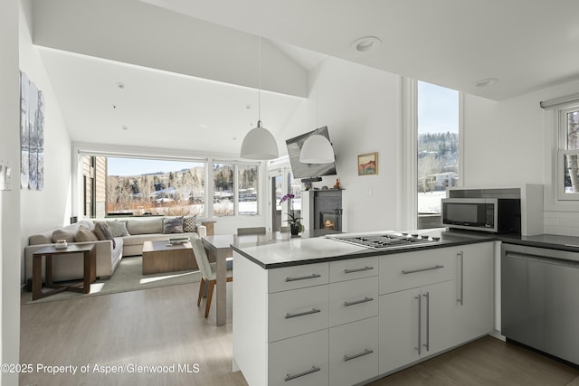 kitchen featuring pendant lighting, white cabinets, kitchen peninsula, stainless steel appliances, and light wood-type flooring