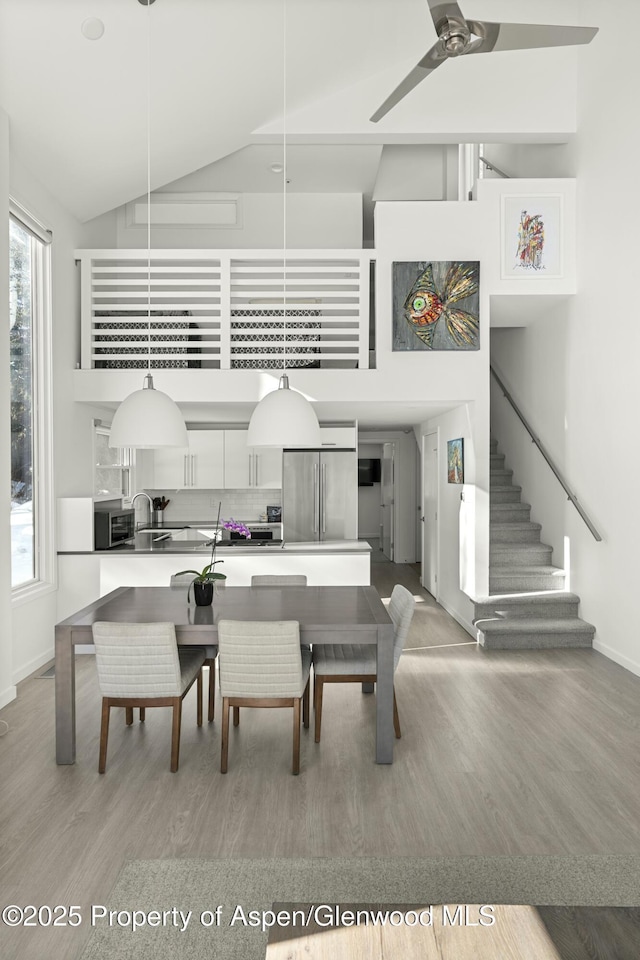 dining room with ceiling fan, wood-type flooring, sink, and high vaulted ceiling