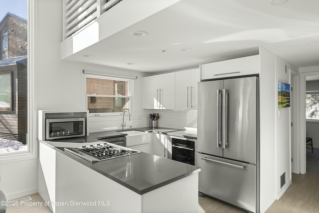 kitchen featuring sink, white cabinetry, stainless steel appliances, tasteful backsplash, and light wood-type flooring