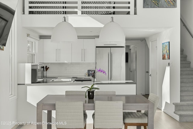 kitchen with high end fridge, sink, white cabinetry, tasteful backsplash, and pendant lighting