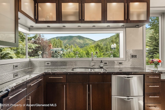 939 E Cooper Ave, Aspen, CO 81611 - kitchen featuring dark brown cabinetry, dishwasher, decorative backsplash, dark stone counters, and glass insert cabinets