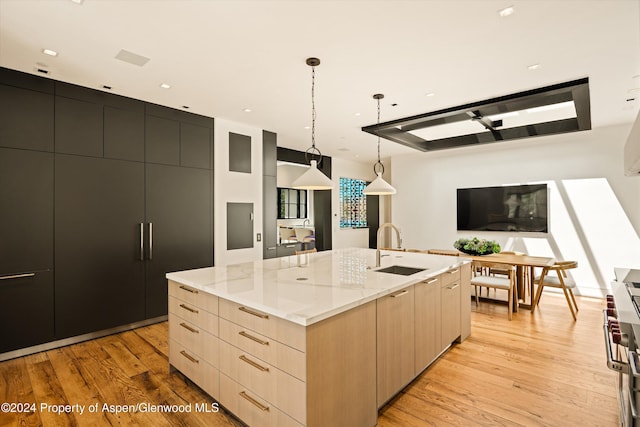 kitchen with a large island with sink, sink, light brown cabinetry, decorative light fixtures, and light hardwood / wood-style floors