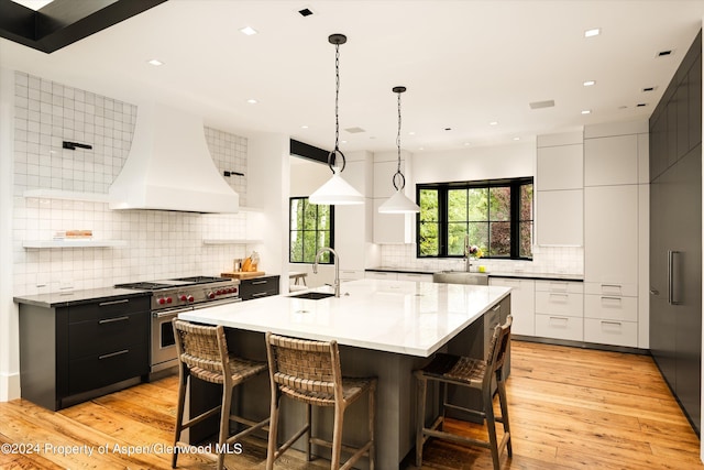 kitchen featuring designer stove, white cabinetry, hanging light fixtures, and custom exhaust hood