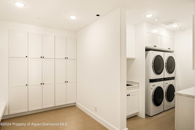 laundry area with washing machine and clothes dryer, stacked washing maching and dryer, light tile patterned floors, and cabinets