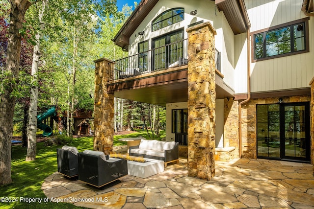 rear view of house featuring a playground, outdoor lounge area, a balcony, and a patio area