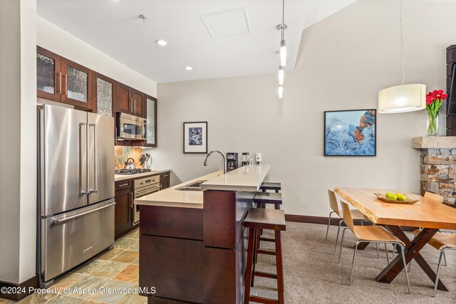 kitchen featuring a kitchen bar, appliances with stainless steel finishes, kitchen peninsula, sink, and hanging light fixtures