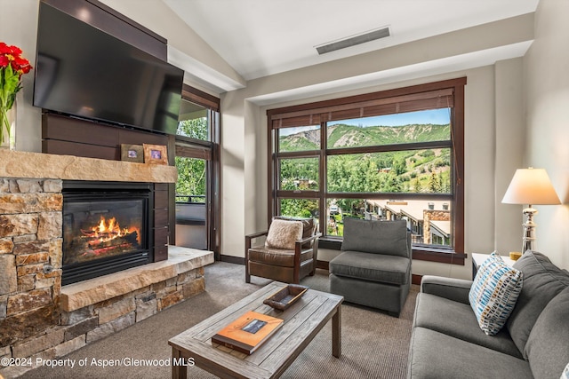 carpeted living room with vaulted ceiling and a stone fireplace