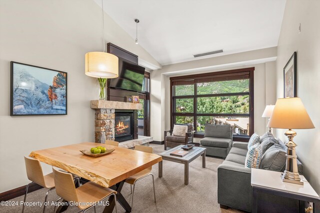 living room with carpet, a stone fireplace, and lofted ceiling