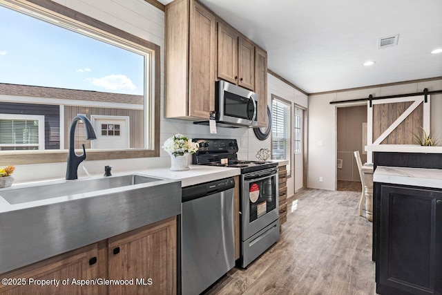 kitchen featuring a barn door, stainless steel appliances, visible vents, light countertops, and light wood finished floors