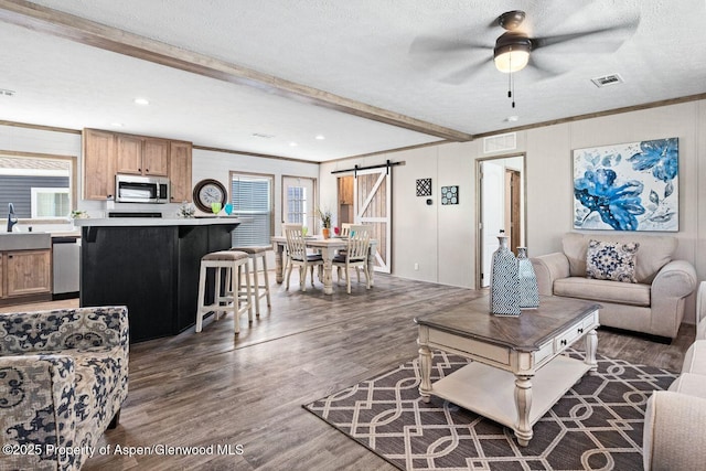 living room featuring a textured ceiling, a barn door, dark wood-type flooring, visible vents, and beamed ceiling