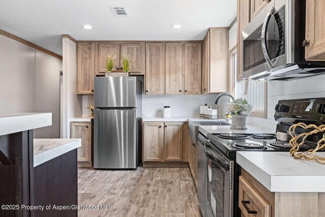 kitchen featuring light countertops, decorative backsplash, appliances with stainless steel finishes, light wood-style floors, and a sink