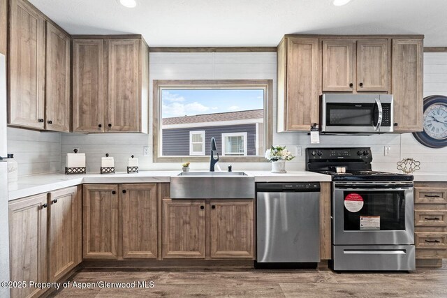 kitchen with wood finished floors, a sink, light countertops, appliances with stainless steel finishes, and decorative backsplash