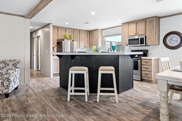 kitchen with light countertops, appliances with stainless steel finishes, a breakfast bar area, and wood finished floors