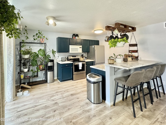 kitchen featuring blue cabinets, kitchen peninsula, a breakfast bar, appliances with stainless steel finishes, and light wood-type flooring