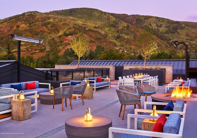 patio terrace at dusk featuring a mountain view and an outdoor living space with a fire pit