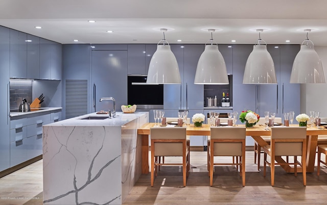 kitchen featuring gray cabinets, a kitchen island with sink, sink, and pendant lighting