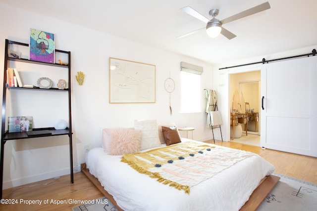 bedroom with a barn door, light hardwood / wood-style floors, ceiling fan, and connected bathroom