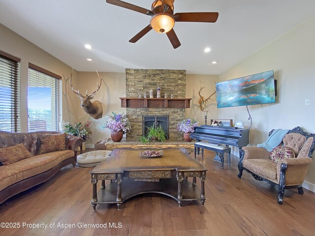 living room with wood finished floors, ceiling fan, a stone fireplace, recessed lighting, and baseboards