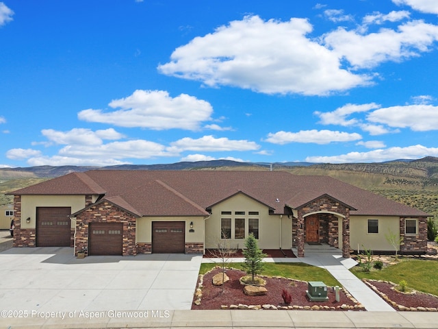 ranch-style home featuring stone siding, a garage, a mountain view, stucco siding, and driveway