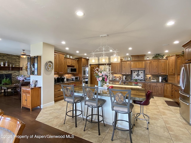 kitchen with stainless steel appliances, a kitchen island with sink, tasteful backsplash, brown cabinetry, and recessed lighting
