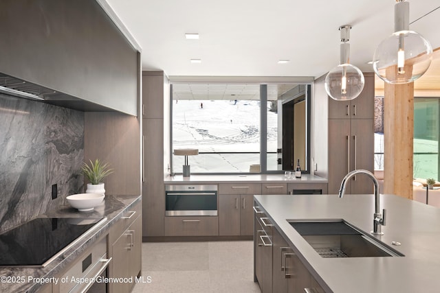 kitchen featuring oven, a sink, tasteful backsplash, black electric cooktop, and hanging light fixtures