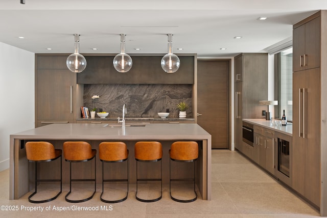 bar with a sink, wine cooler, stainless steel oven, decorative light fixtures, and tasteful backsplash