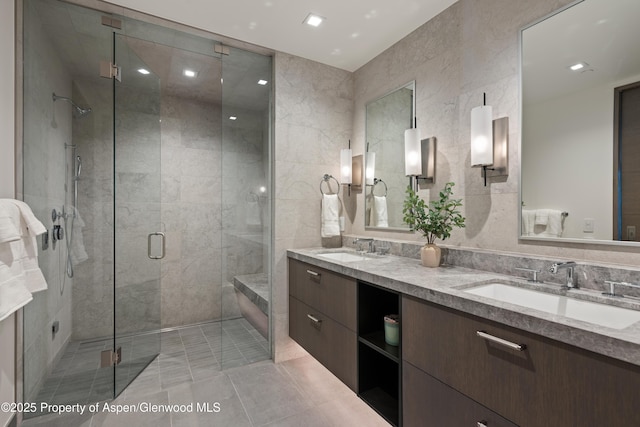 full bathroom with a sink, tile walls, a shower stall, and double vanity