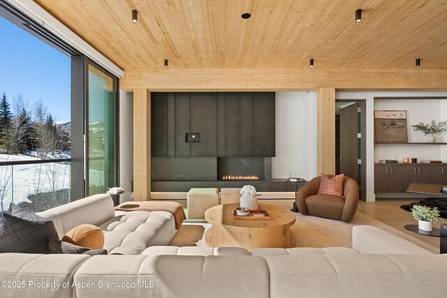 living room featuring a lit fireplace and wood ceiling