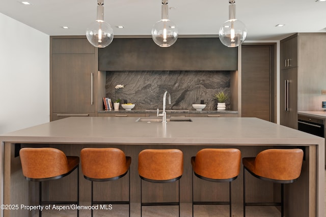 kitchen with modern cabinets, a sink, backsplash, a breakfast bar area, and light countertops