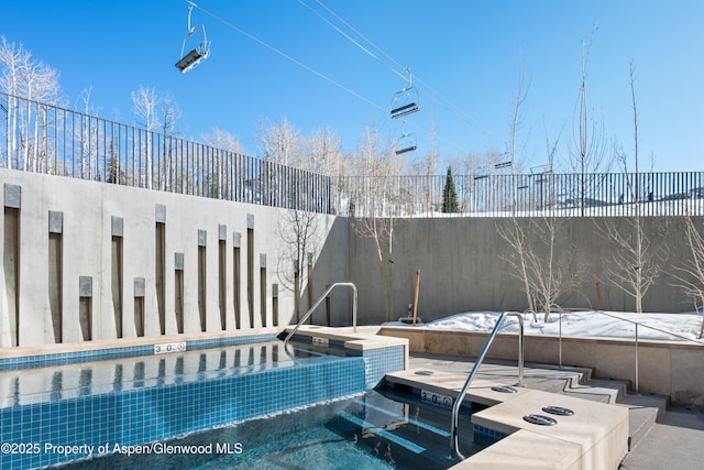 view of swimming pool with fence and a hot tub