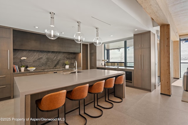 kitchen with a sink, decorative backsplash, light countertops, a kitchen bar, and modern cabinets