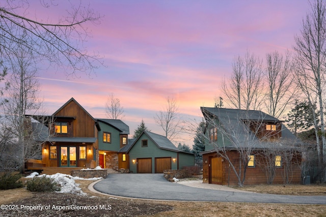 rustic home with an outbuilding, an attached garage, driveway, stone siding, and board and batten siding