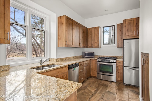 kitchen with stainless steel appliances, light stone counters, a sink, and brown cabinets