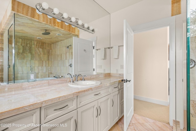 bathroom with a tile shower, vanity, and baseboards