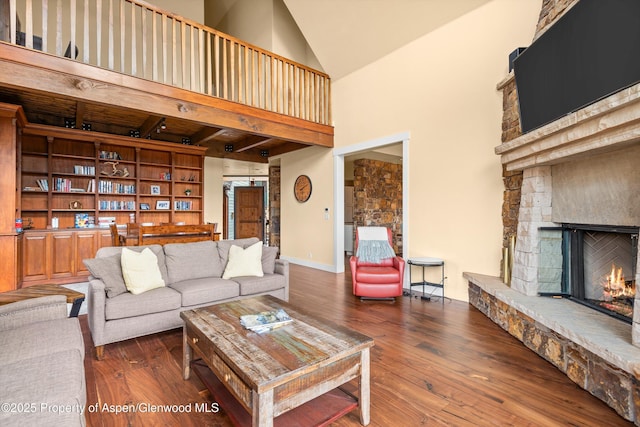 living area with a high ceiling, baseboards, a stone fireplace, and hardwood / wood-style floors