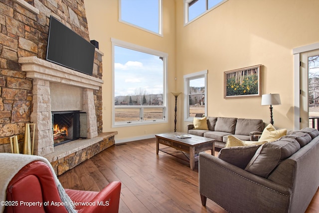 living room featuring a high ceiling, wood-type flooring, a fireplace, and baseboards