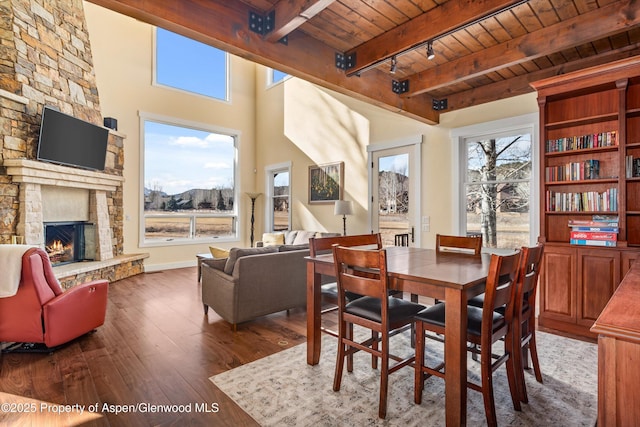 dining area with beam ceiling, a fireplace, rail lighting, wood ceiling, and hardwood / wood-style floors